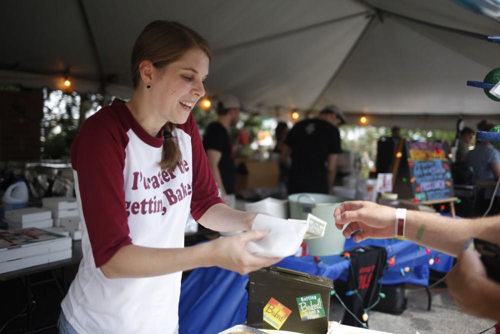 Tyler Ness, a baker at Baked!, hands cookies to a customer during Taste of Bloomington on June 20, 2015. The Baked! table was lined with a variety of cookies available for purchase.  