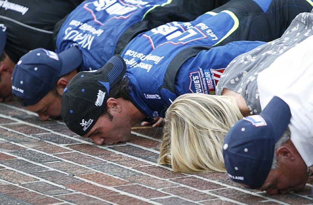 Jimmie Johnson (center), along with his wife Chandra Johnson, crew chief Chad Knaus and car owner Rick Hendrick (far right) kiss the bricks following the No. 48 Lowes’ team’s victory at the Allstate 400 at the Brickyard Sunday afternoon in Indianapolis.