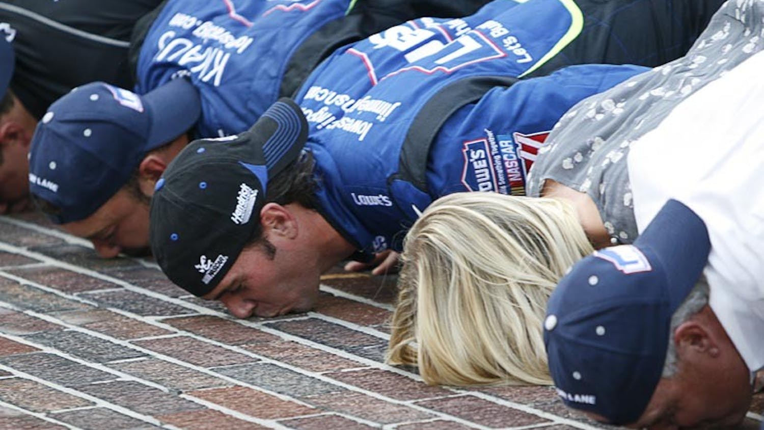 Jimmie Johnson (center), along with his wife Chandra Johnson, crew chief Chad Knaus and car owner Rick Hendrick (far right) kiss the bricks following the No. 48 Lowes’ team’s victory at the Allstate 400 at the Brickyard Sunday afternoon in Indianapolis.