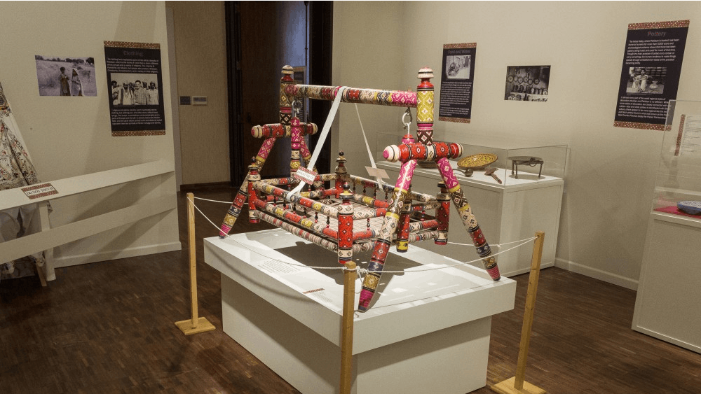 A colorful child’s cradle sits in the center of the Snapshot of Pakistan exhibit at the Mathers Museum. The cradle was made through a labor intensive process which includes shaping the wood on a lathe and then applying various layers of color before the artist etches in a design of their choice.&nbsp;