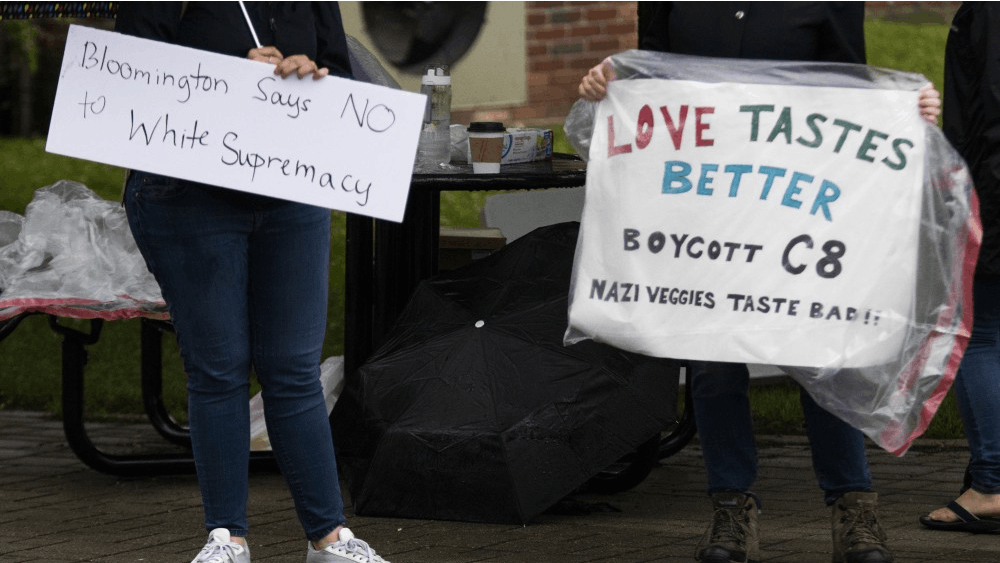 People hold protest signs June 15 at the Bloomington Farmer’s Market. The signs read, “Bloomington says no to white supremacy&quot; and “Love tastes better. Boycott C8. Nazi veggies taste bad!!”