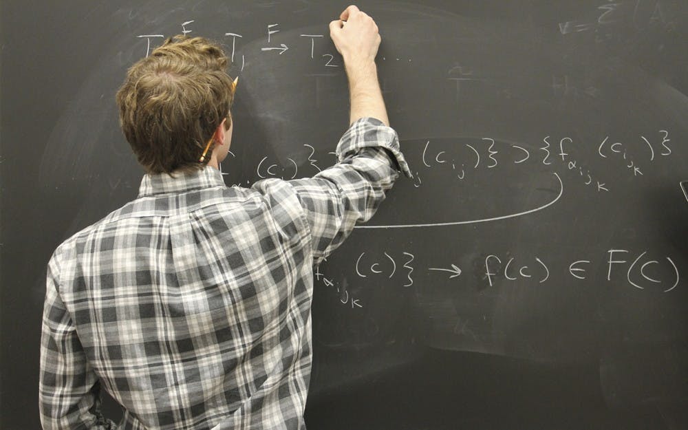 Grant Schumacher, an undergraduate majoring in math and physics, explains a complicated math concept using equations during a meeting with his research group on Wednesday.