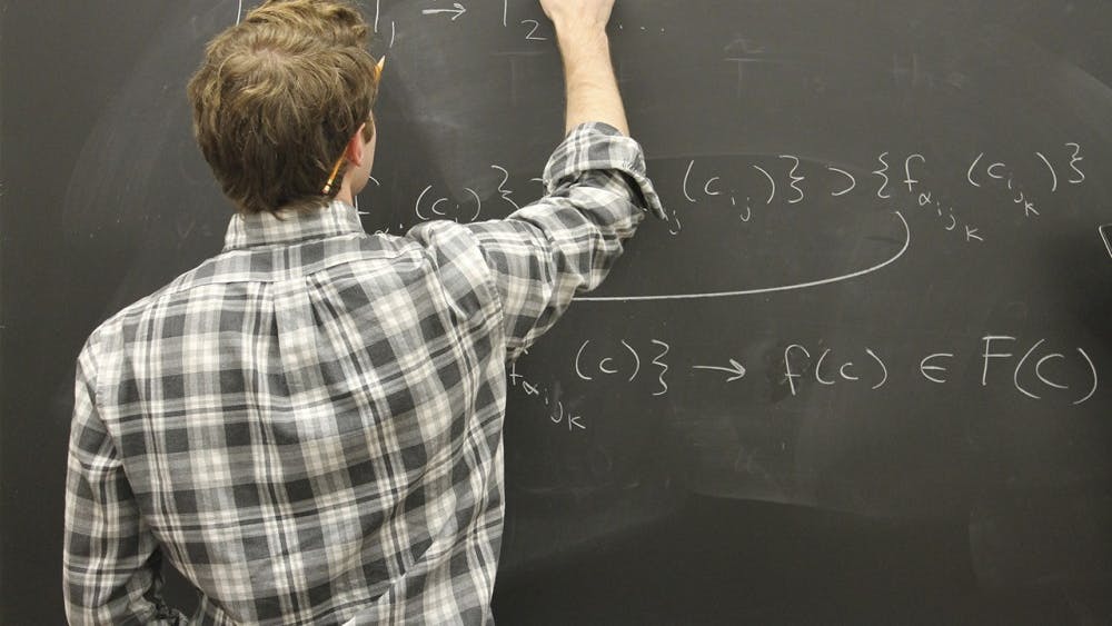 Grant Schumacher, an undergraduate majoring in math and physics, explains a complicated math concept using equations during a meeting with his research group on Wednesday.