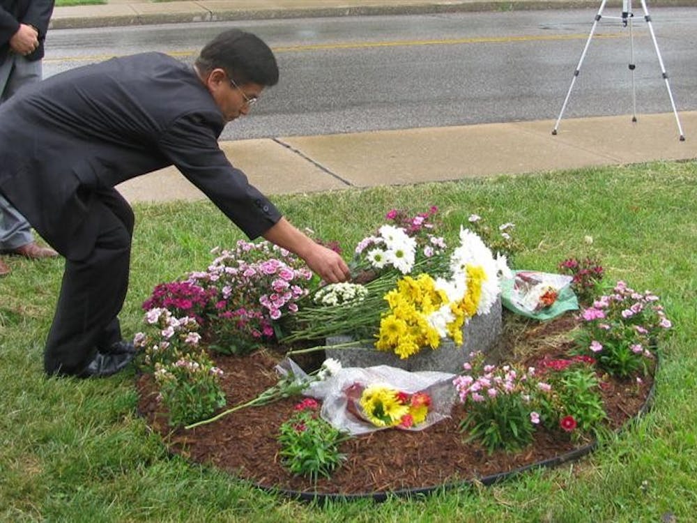 Pastor Gi-Chae Lee of the Korean United Methodist Church places a flower on a memorial for IU graduate student Won-Joon Yoon on Saturday. Yoon was killed 10 years ago after a white supremacist shot him outside of the church.                                 