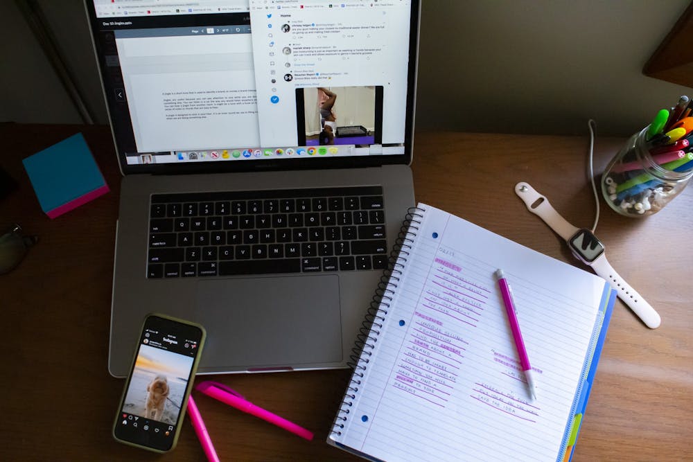 一名学生的桌子上摆满了笔记、笔记本电脑和一部显示社交媒体帖子的手机。