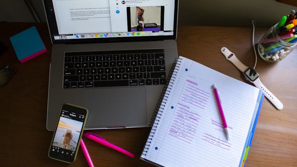 Notes, a laptop and a phone displaying social media posts fill a student’s desk.