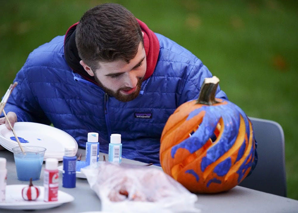 <p>Freshman Tanner Graves decorates pumpkins while chatting with friends during Central’s Creepy Carnival Saturday evening outside of Teter Quadrangle. The event featured laser tag, free food catered by Residential Programs and Services Dining and an outdoor movie screening of the 1984 film Ghostbusters.</p>