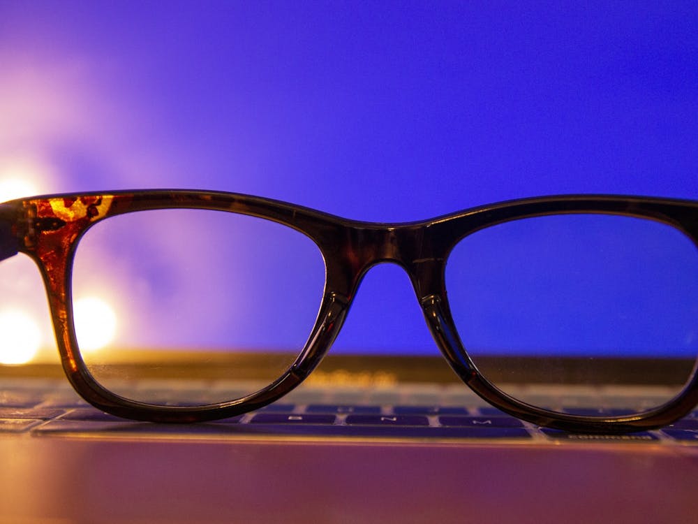 A photo illustration shows a pair of blue light glasses resting in front of a laptop screen.
