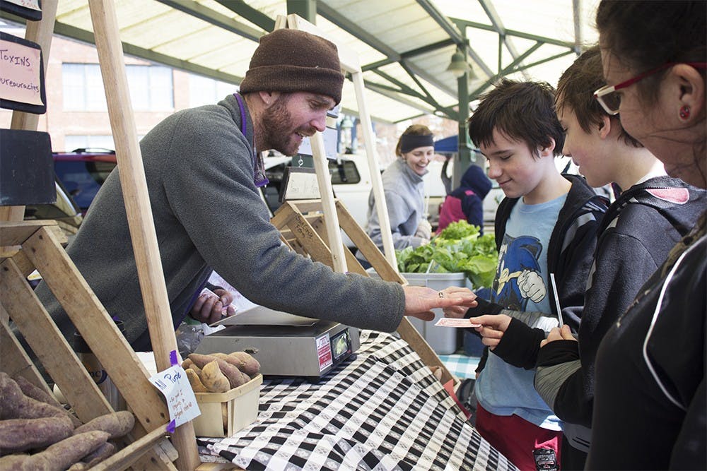 Laura Reagan, IU alum, and her sons Korbyn Reagan-Walls and Jarek Reagan-Walls watch a magic card trick from Paul Nord on Saturday. Nord has been sellling produce from Sun Circle farm at the farmers market for several years.