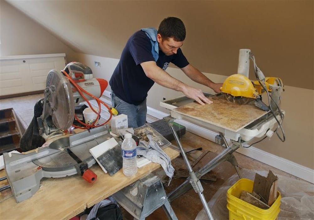 Sgt. John Obermeier, a member of the Jeffersonville, Indiana Fire Department, concentrates on cutting tile for a bathroom in Police Officer Keith Broady's home on Tuesday. Broady had started the work before he was recently wounded, and now firefighters are helping to complete the renovation.   