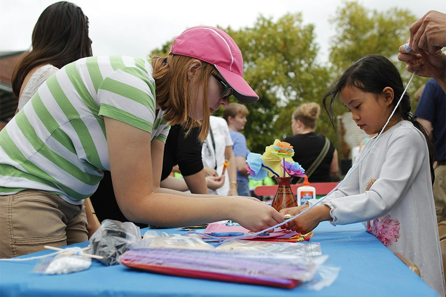 Mary Bolander, a volunteer with the Bloomington Sister Cities program helps Sasha Luhur, age 6, make a craft with yarn and popscicle sticks during the "Fiesta del Otoño" at Showers Plaza during the Farmer's Market Saturday.