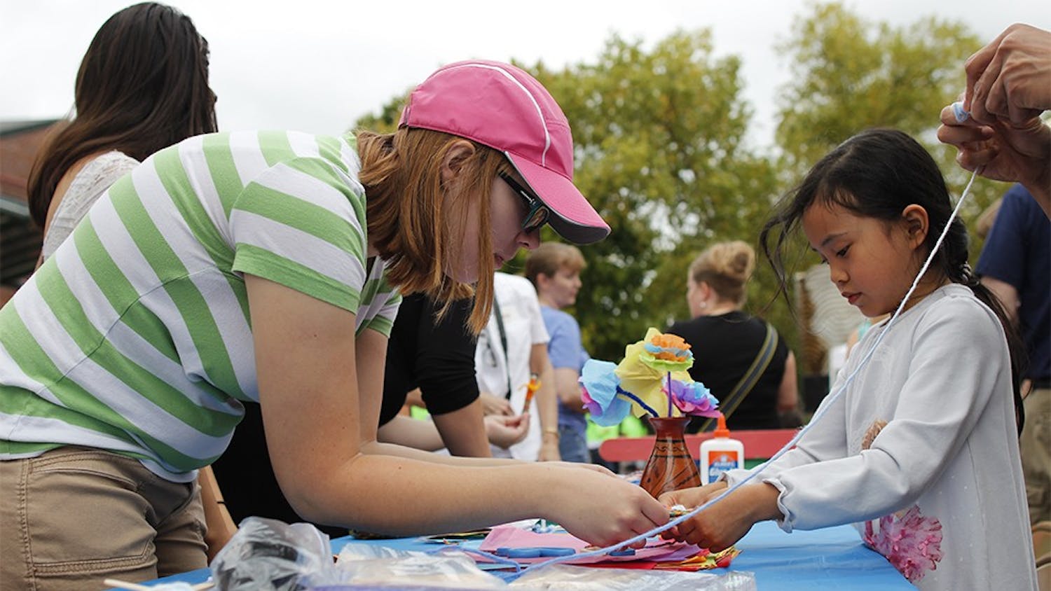 Mary Bolander, a volunteer with the Bloomington Sister Cities program helps Sasha Luhur, age 6, make a craft with yarn and popscicle sticks during the "Fiesta del Otoño" at Showers Plaza during the Farmer's Market Saturday.