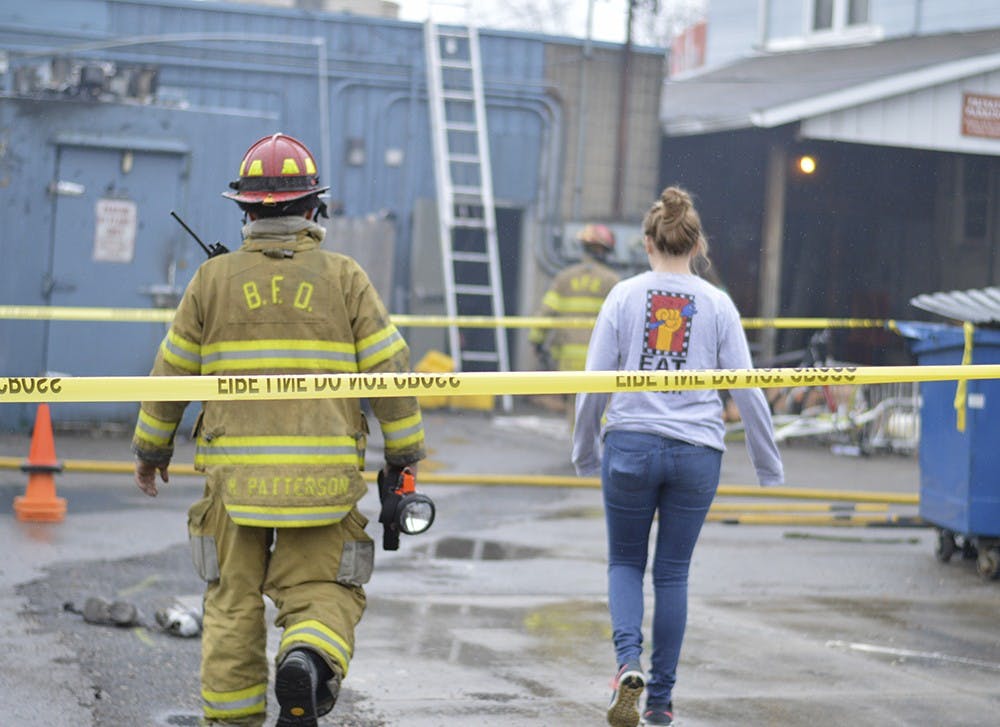 Firefighters take Village Deli staff members back into the restaurant one at a time to get the belongings they left behind in the restaurant Sunday.