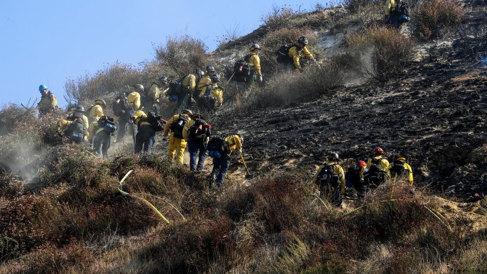 Firefighters clear brush and mop up the hillside along the 14 Freeway, which is closed to traffic through Newhall Pass due to the Saddle Ridge fire Oct. 11 in Newhall, California. 