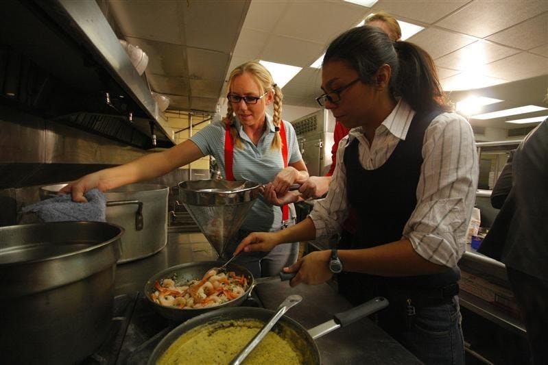 Senior Amber Lindgren moves a pot on the stove out of the way while holding a colander of shrimp working with Freshman Marina Karamanis Friday evening in the Tudor Room kitchen at the Indiana Memorial Union. Members of the women's golf team participated in an Iron Chef event, where members split up in to teams and cooked food to be judged by Coach Bill Lynch and other members of IU Athletics coaching staffs.