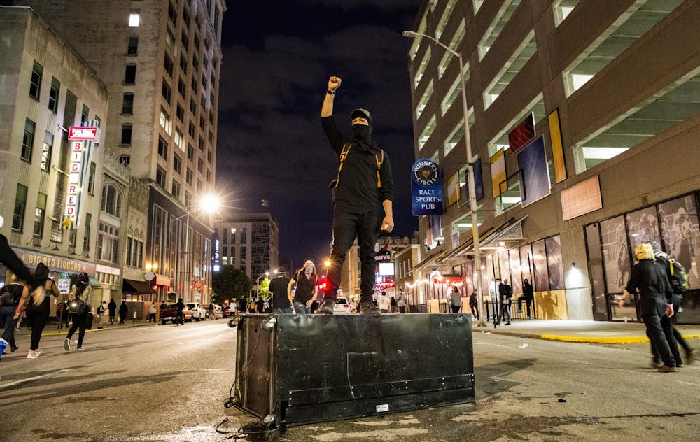 <p>A protester stands on a knocked over vending machine May 30 in downtown Indianapolis. Protesters ran around the streets avoiding police tear gas.</p>