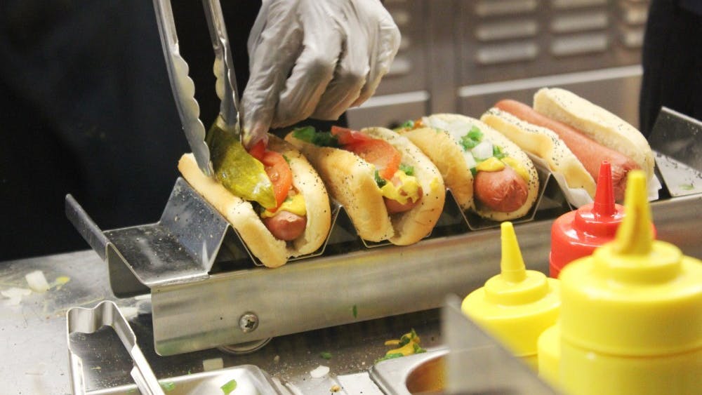 Workers at Portillo&#x27;s carefully place the toppings on hot dogs to fulfill orders.