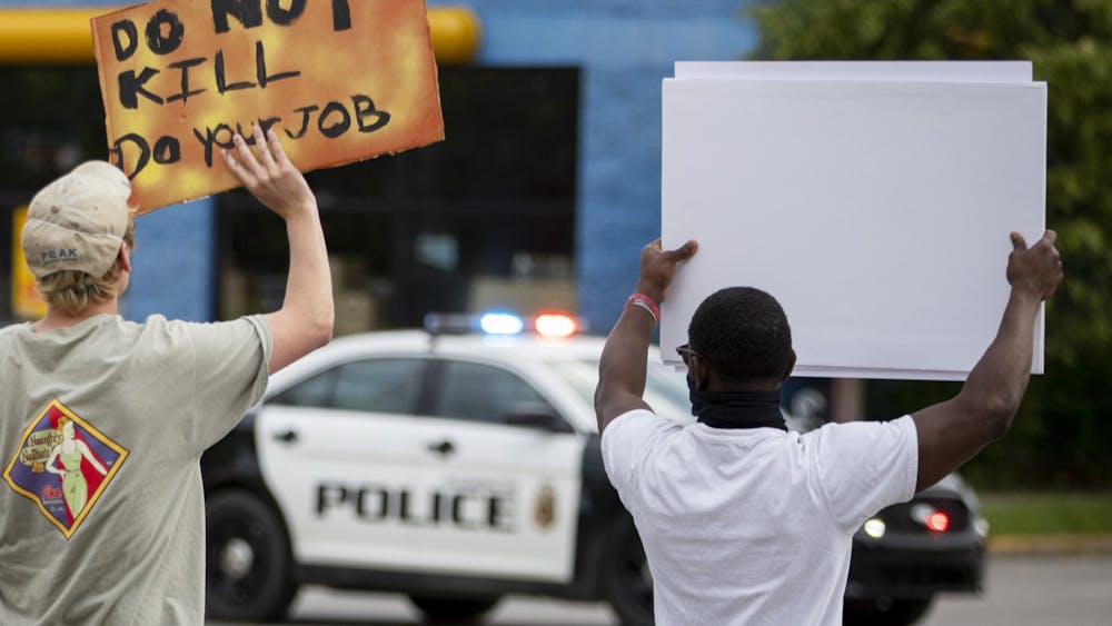 Protesters hold signs as they walk toward police cars June 1 on Third Street.