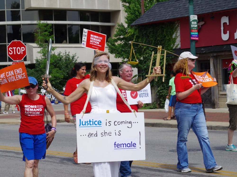 A woman dressed as the female embodiment of justice walks down Kirkwood Avenue as part of the Bloomington Fourth of July Parade. She was marching with the Moms Demand Action For Gun Sense in America, a group which advocates for better gun control laws.