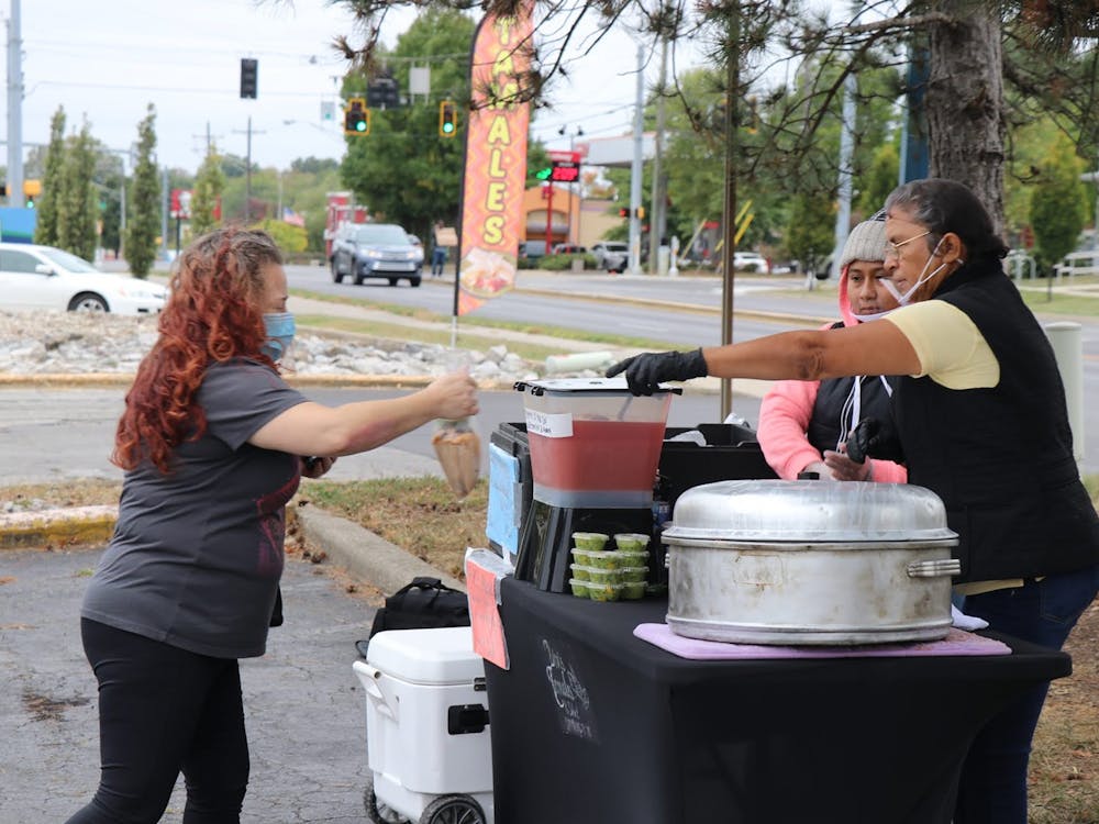 Bivianna Torres hands a tamale to a customer Sept. 26 outside Bloomingfoods East. Torres said the pandemic has slashed business nearly in half for her.﻿
