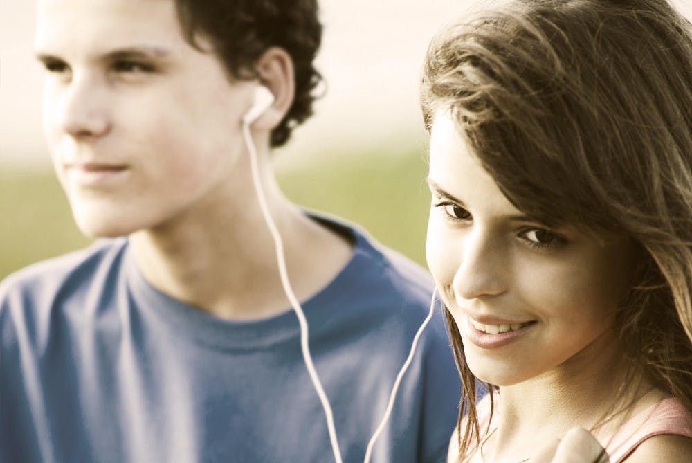 Teens sharing earphones, listening music outdoor. Summer time.  Image is captured in 12 bit RAW and processed in Adobe RGB color space.
