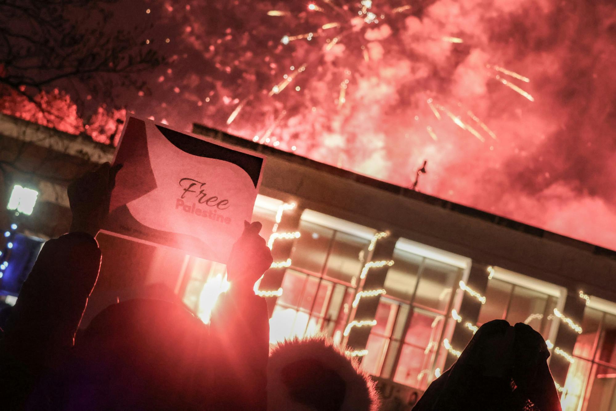Students held up flyers demanding freedom for Palestine as the fireworks set off at the end of the 2023 Lighting of the Quads.