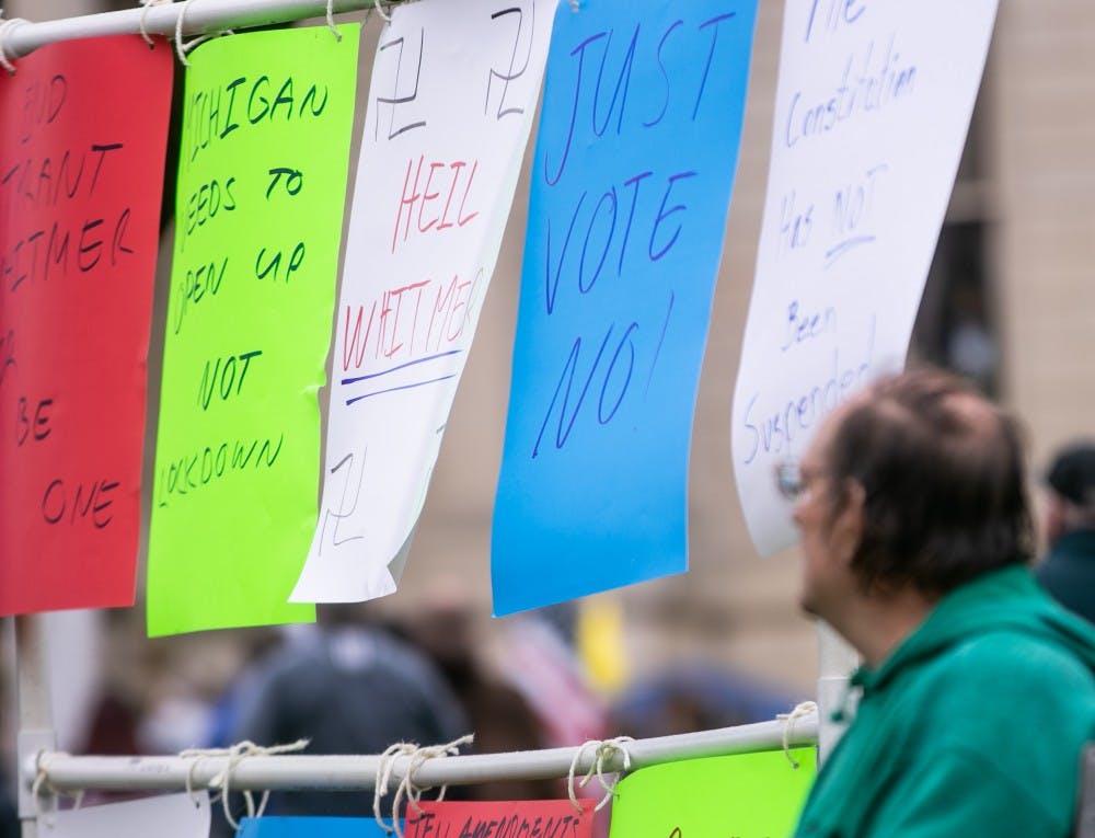 A man sits next to his signs at the rally at the Capitol April 30, 2020 in Lansing.