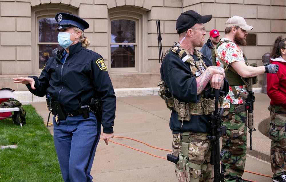 A police officer walks past a man in tactical gear at the rally at the Capitol April 30, 2020 in Lansing.