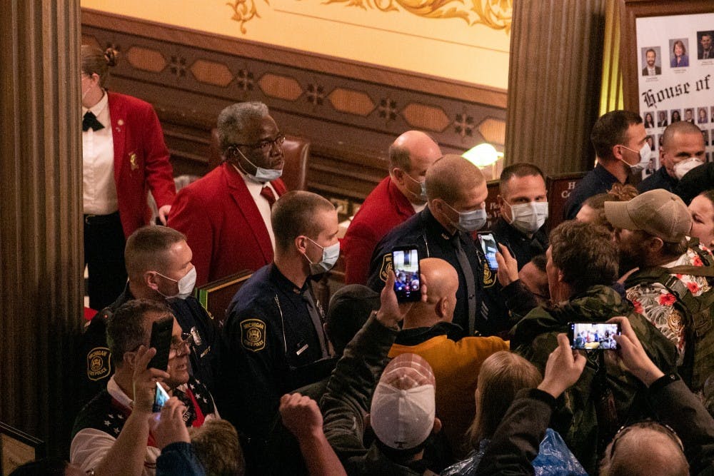 A crowd yells at police officers and employees guarding a door to the House floor at the protest in the Capitol April 30, 2020 in Lansing.