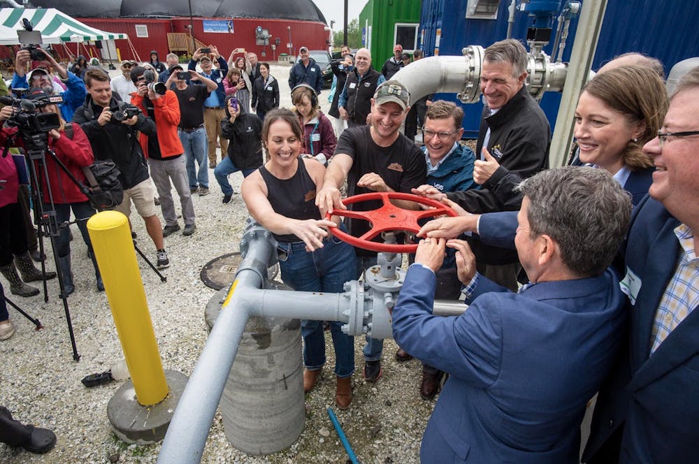 <p>Goodrich Farm Co-Owner Danielle Goodrich Gingras, Goodrich Farm Co-Owner Chase Goodrich, Vermont Gas Systems CEO Neale Lunderville, Vermont Governor Phil Scott, Vermont Lieutenant Governor Molly Gray, and Middlebury college Treasurer David Provost open the valve between the biodigester and its pipeline in July. (Courtesy of Glenn Russell/VTDigger)</p>