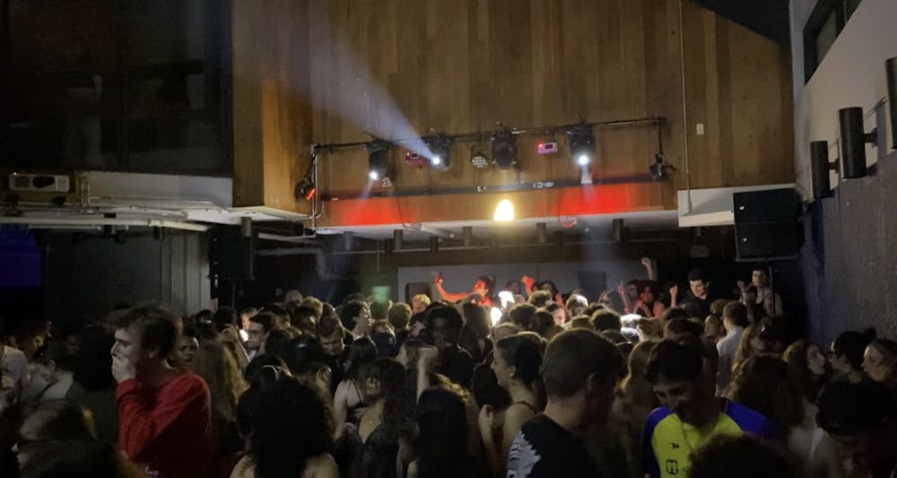 Floor view photo of students at the Laylit rave with the DJ booth in the background.