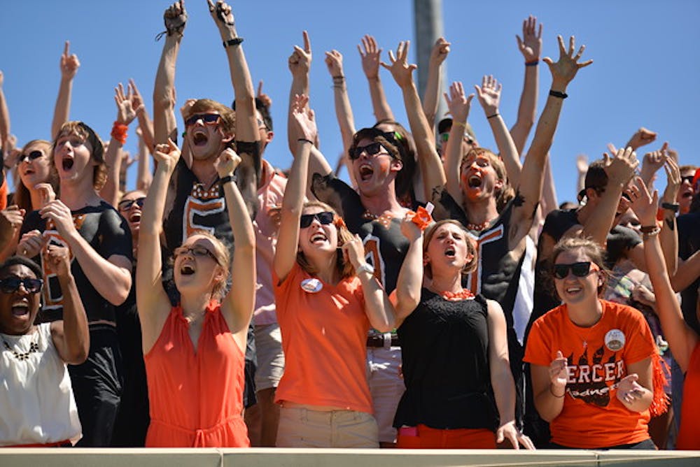 A group of spirited students, some representing the organization Mercer Maniacs, cheer on a Mercer football game.