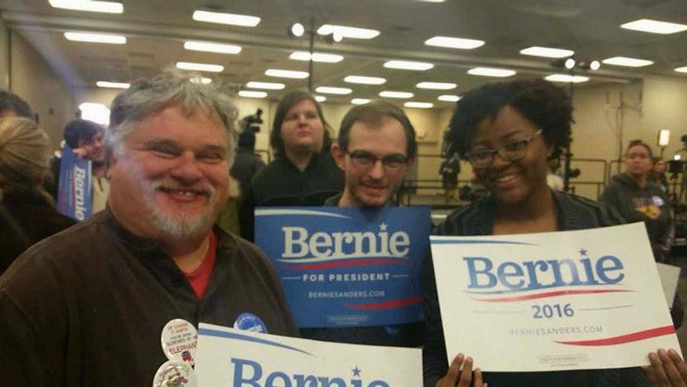 Chris Grant, Drew Bryant, and Desirrae Jones hold up signs for Bernie Sanders during their time at the Iowa caucus.
