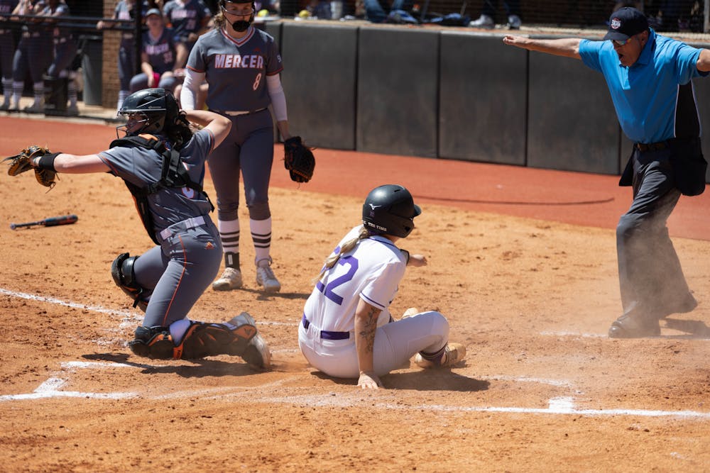 A Furman player slides into home plate, evading the tag, while Bears catcher Tori Ash attempts to throw out a different runner. The Bears would go on to lose the game 2-4.