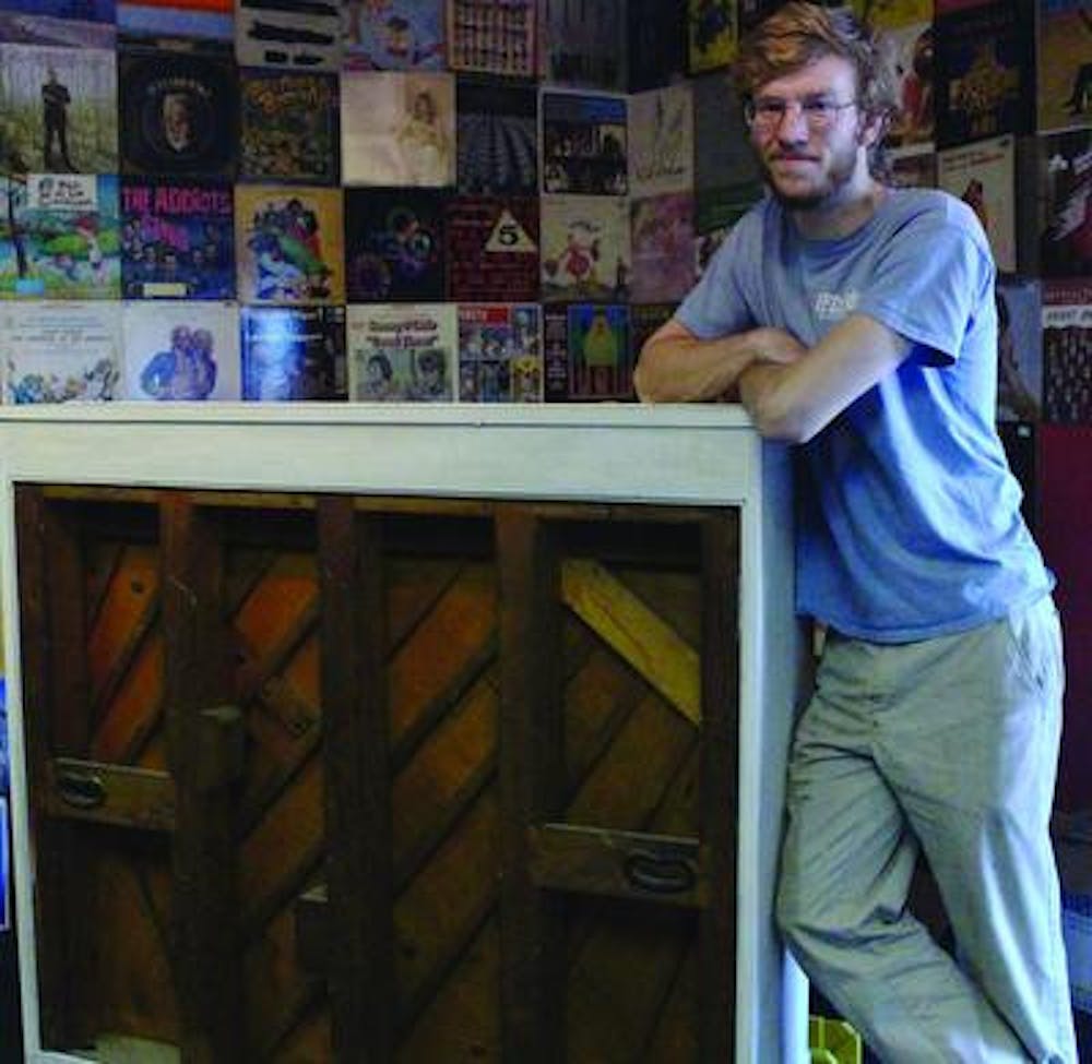 Andrew Eck, 5/4 Music Space Co-owner, stands next to historical piano at the business' brick in mortar on Walnut Street.
