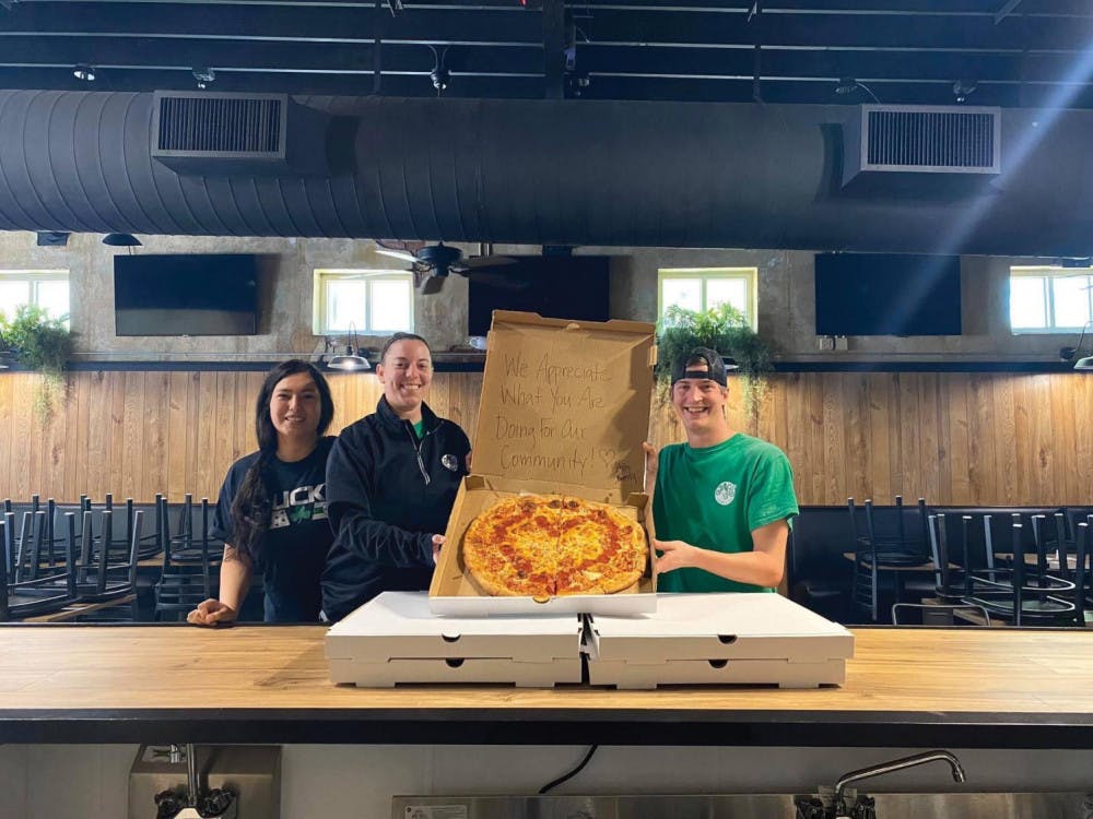 Dahlia Sanchez, Lisa Williams, and Andrew Gates hold a pizza box that reads “We appreciate what you are doing for our community!”