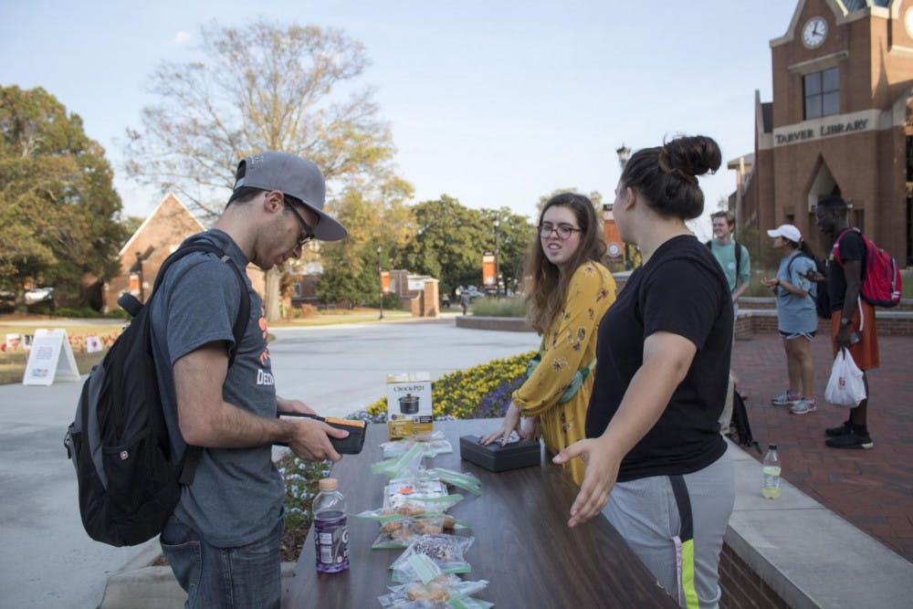 Avery Davis, junior (middle), and Amina Mohamed, sophomore (right), help Justin Hanson, senior (left) buy a pastry for RHA Greekments' Pastries for Pancreatic Cancer outside Stetson Hall on Nov. 7, 2017. 
