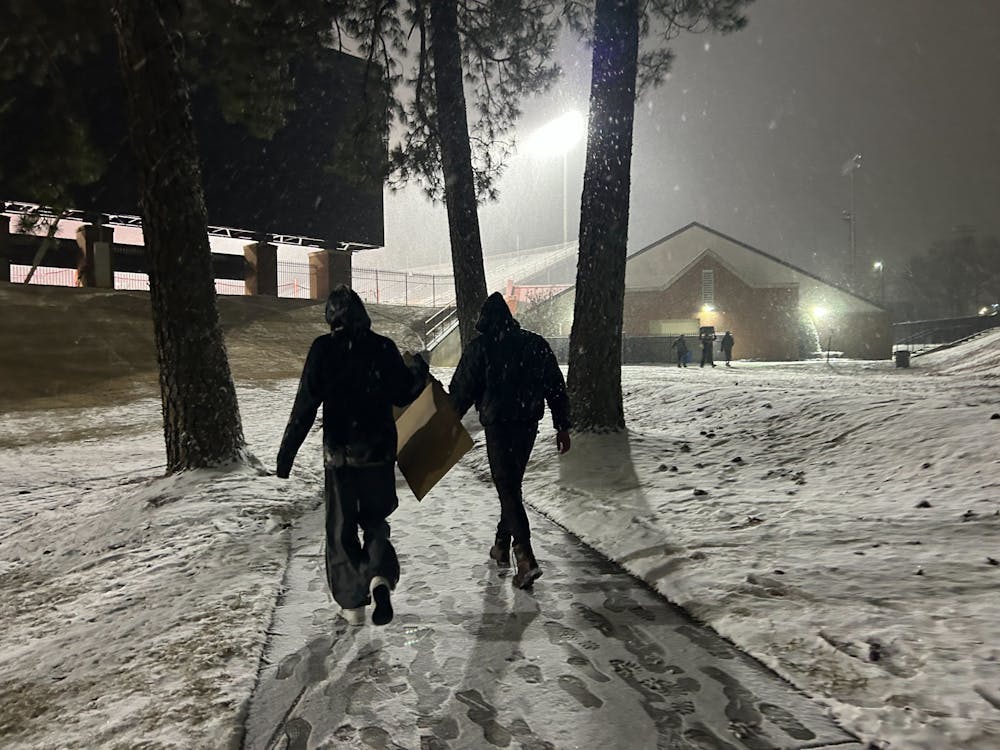 <p>Two Mercer students walk through the snow near Black Field with a piece of cardboard. Many students used cardboard boxes, pool floats and more as makeshift sleds on Jan. 21, 2024.</p>