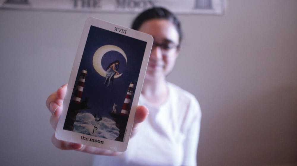 Emily Rose Thorne holds The Moon tarot card.