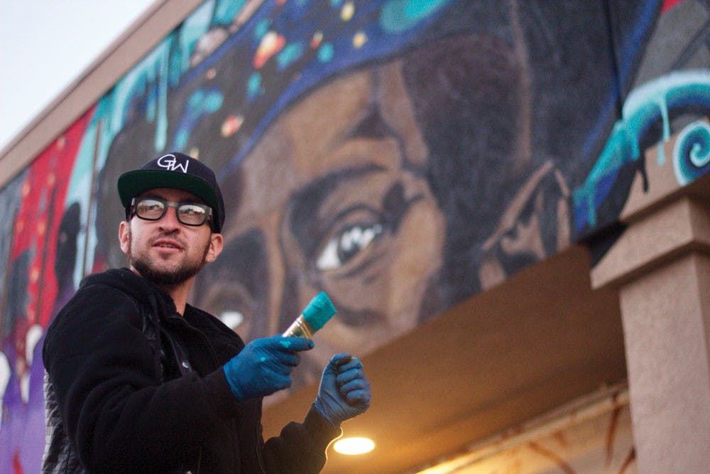 Artist Joereal Numina paints a mural on the exterior wall of Indigo Salon on Coleman Avenue in 2017. The mural is named “Cultivating New Tones on the Spectral Stage of History.”