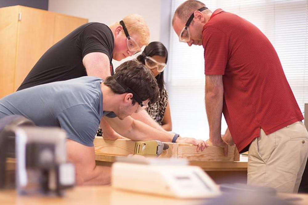 Mercer students Brent Lunsford (top left) and Andrew Wilzman (bottom left) work on a catapult with professors Chamaree de Silva and Jeff Pullen. As a part of a Research that Reaches Out Summer Program, they designed, built, and delivered low-cost mobile labs for Central High School.