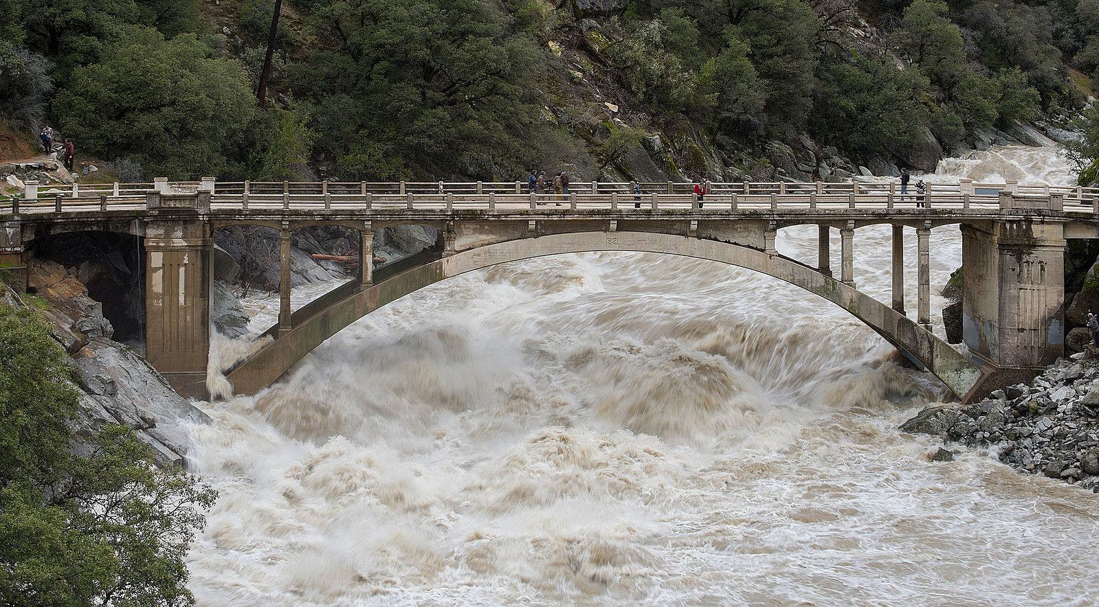 Just one month into the new year, people are already experiencing intense flooding and destruction across California as homes and schools are left as debris (Photo courtesy of Wikimedia Commons / “Flood under the Old Route 49 bridge crossing over the South Yuba River in Nevada City, California” by Kelly M. Grow/ California Department of Water Resources. PD California. January 9, 2017). 