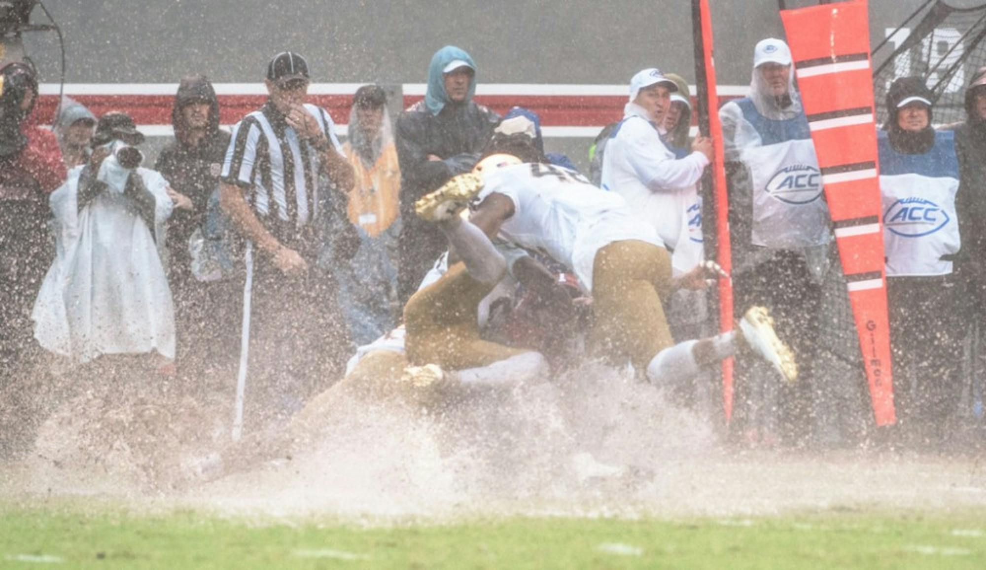 Irish freshman defensive lineman Julian Okwara, top, joins freshman cornerback Julian Love, middle with cleats up, and sophomore running back Dexter Williams in tackling the N.C. State kick returner Saturday in the Irish loss. This was a common sight throughout the day as players landed in puddles or slid for five yards after falling or diving.