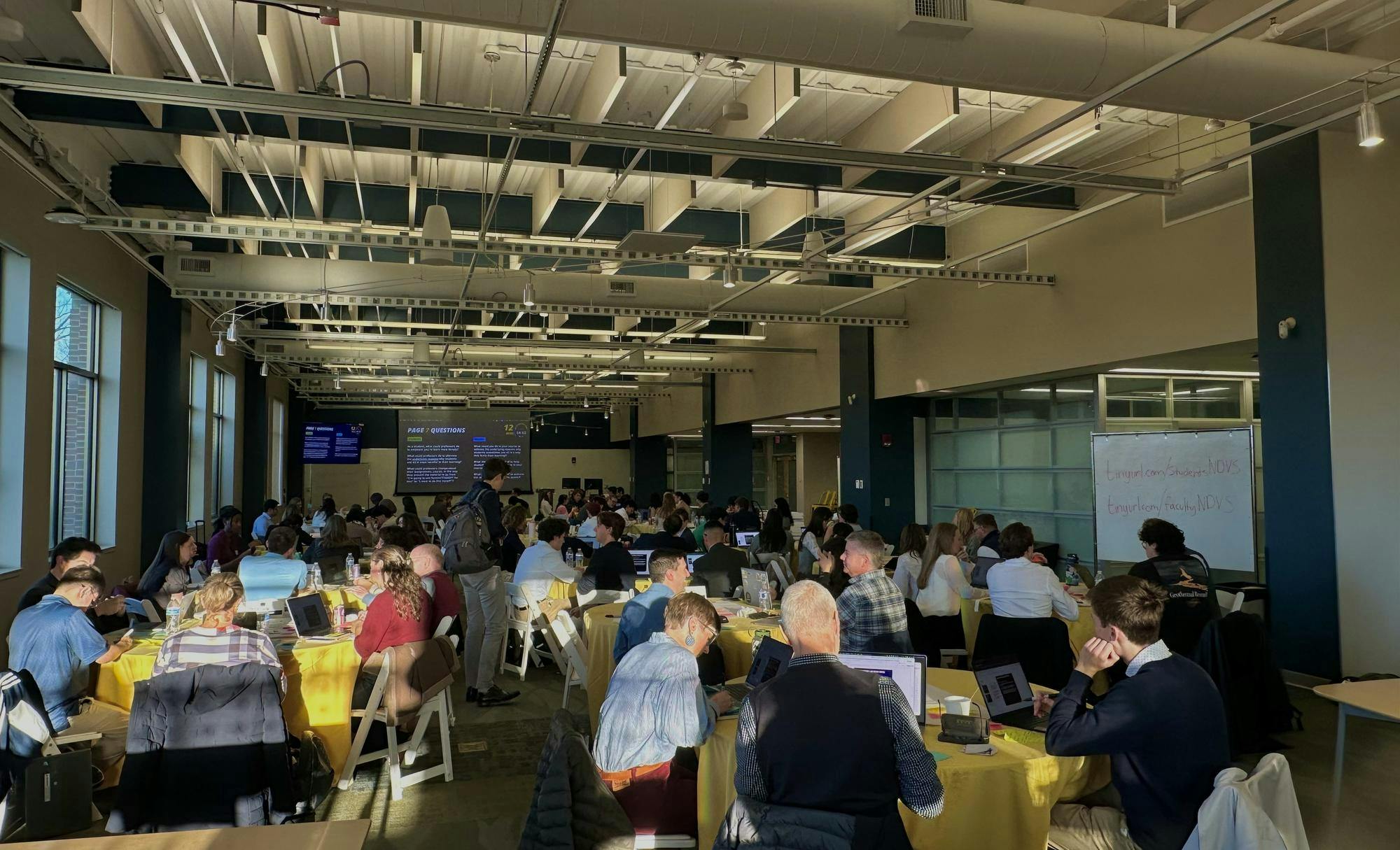 Students and faculty sit in various tables for summit on AI
