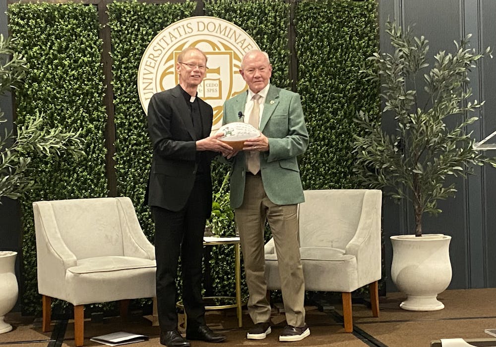 University President Fr. Robert Dowd presents signed football to former chairman of the Joint Chiefs of Staff