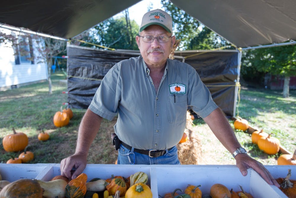 Tom Weekly poses in front of some of the pumpkins and gourds he harvested on his farm, Weeklyville Farm, in Athens, Ohio, this fall. This crop season has had different impacts on farmers, for Weekly, due to low amounts of rainfall his crop has produced less pumpkins. (HANNAH SCHROEDER | FOR THE POST)