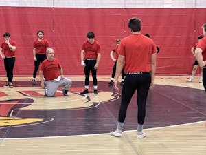 Assistant coach Doug short kneels on a wrestling mat while Otterbein wrestlers watching during a practice session. 