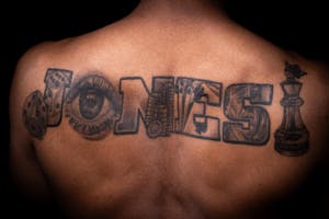 A mans upper back tattoo that says his last name, Jones.