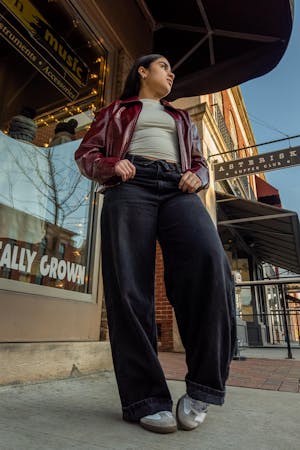 Dark haired girl with purple jacket, jeans and white shirt looking away from the camera posing in front of a music store.