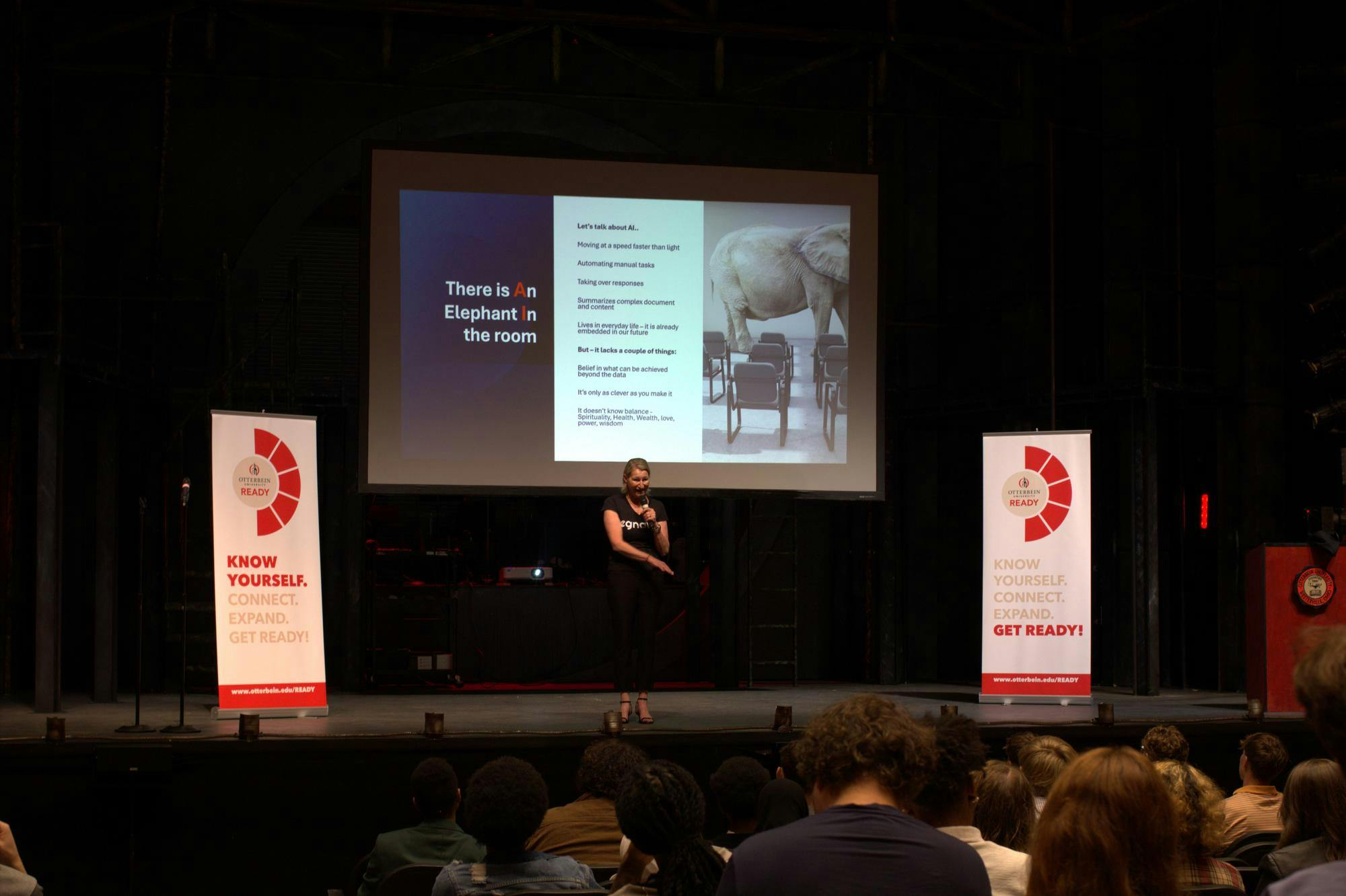 A woman speaks on a stage. Behind her is a presentation slide about AI.